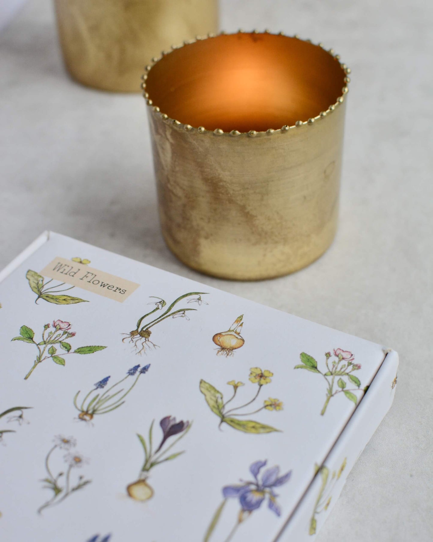 A lit tealight within a brass holder, shown next to an illustrated box of scented tealights.