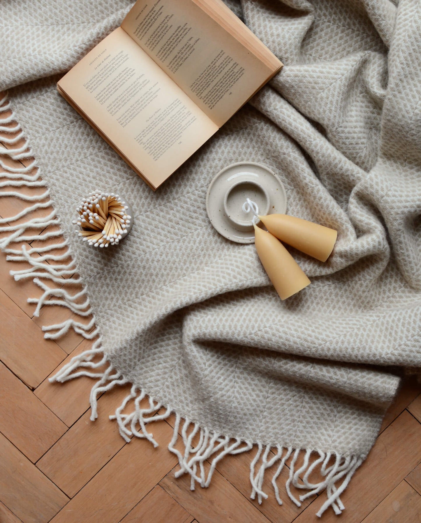 An oatmeal beehive pattern blanket on a wooden floor, with a book.