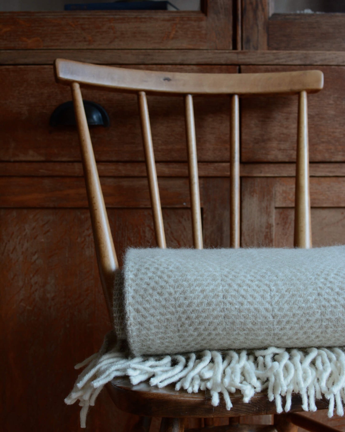 An oatmeal beehive pattern blanket, golded on a wooden chair.