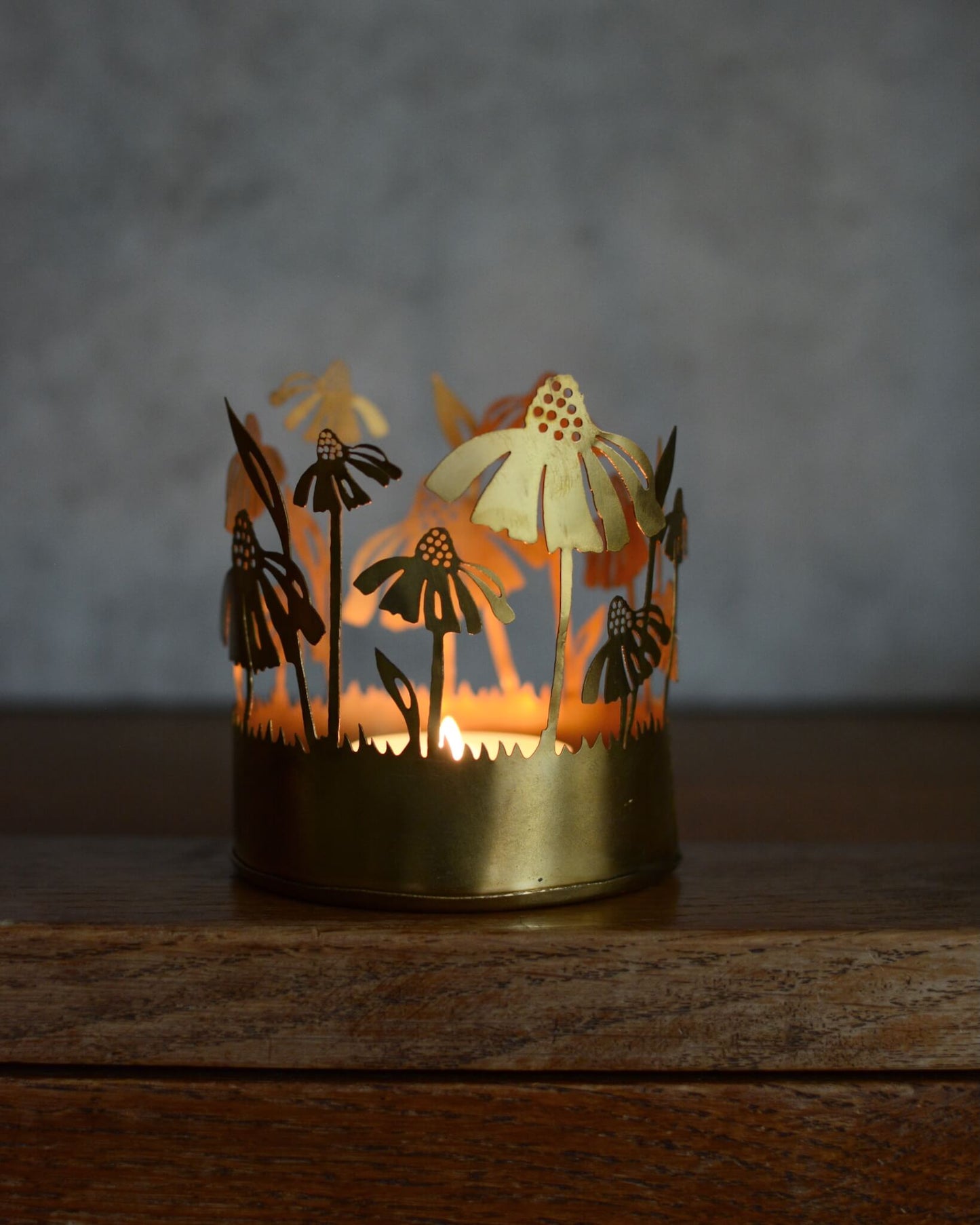 Brass tealight candle holder with floral design, illuminated by candlelight.