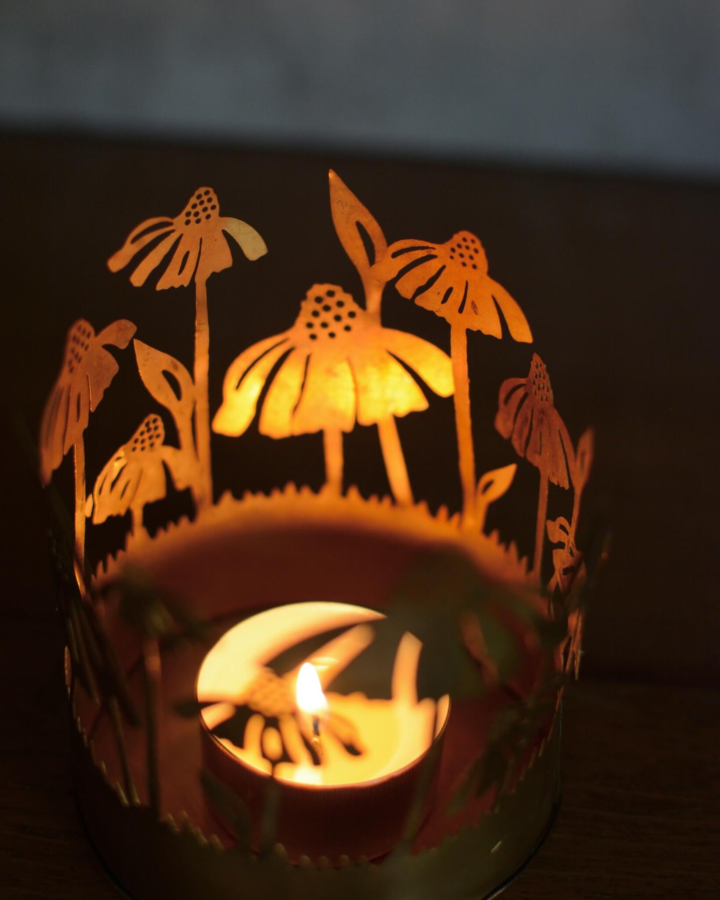 Decorative brass candle holder with floral cutout design, lit from within.
