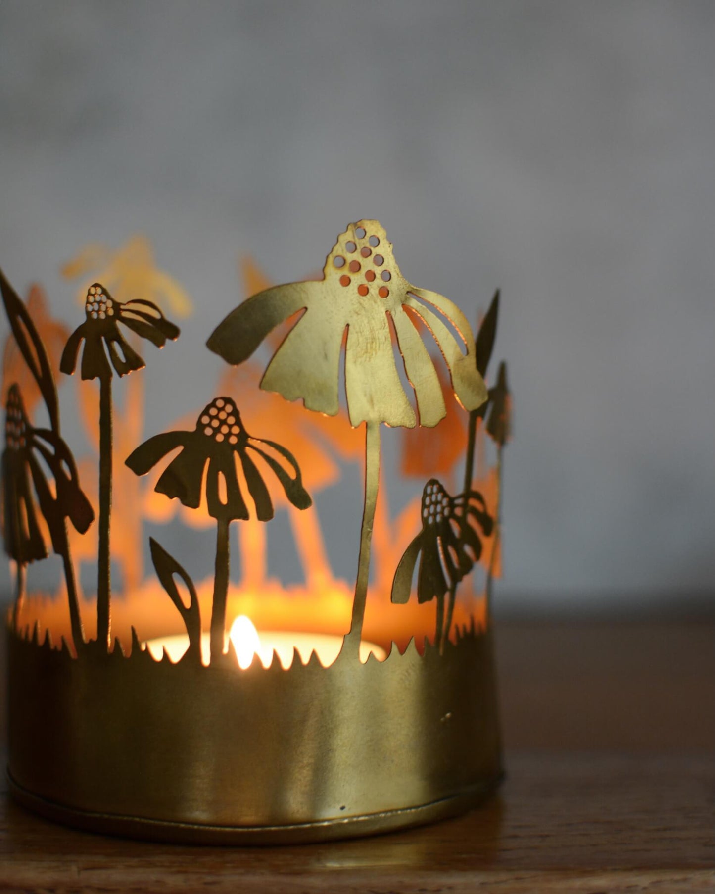Brass tealight candle holder with floral design, illuminated by candlelight.