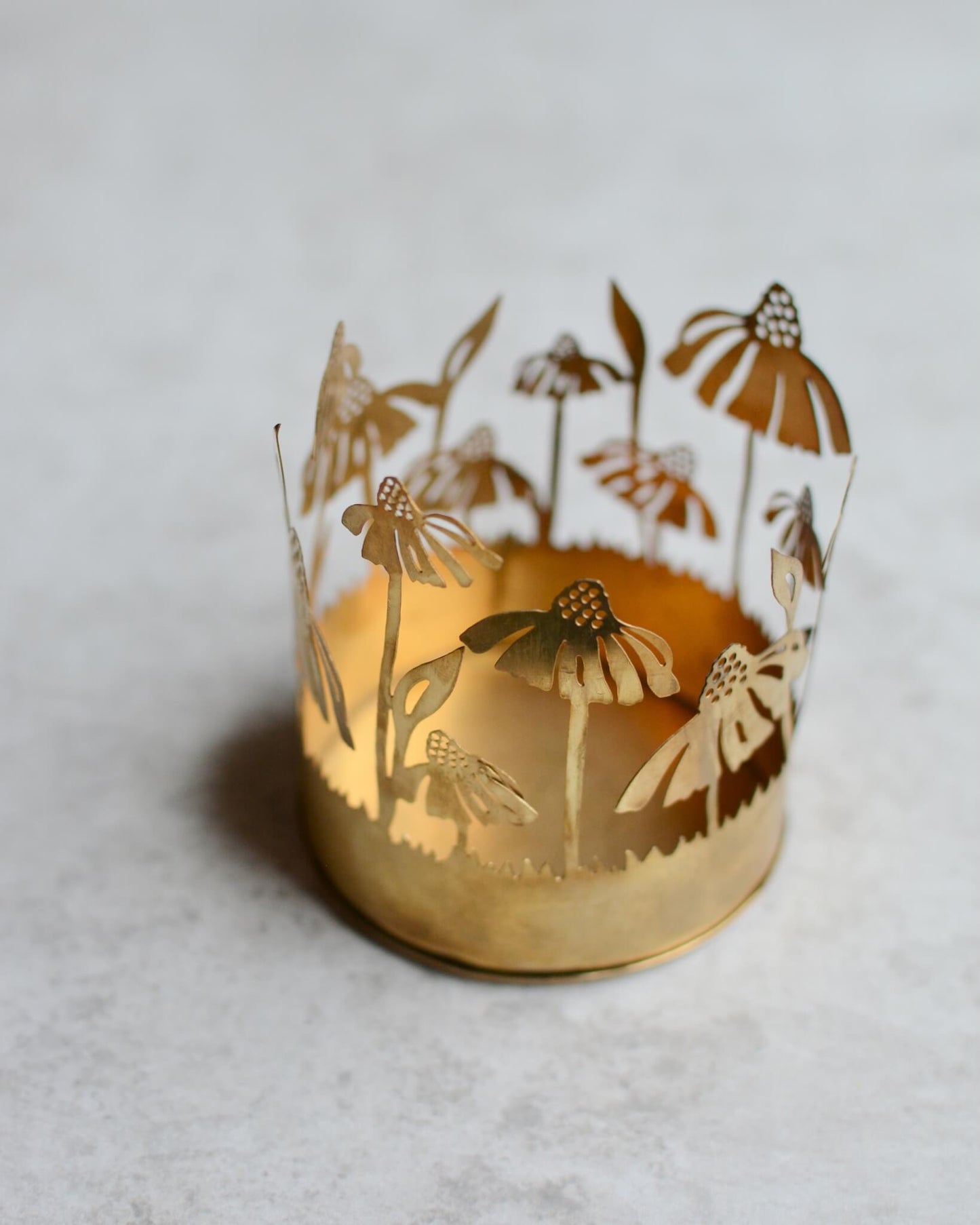 Brass tealight candle holder with floral design on a white background.