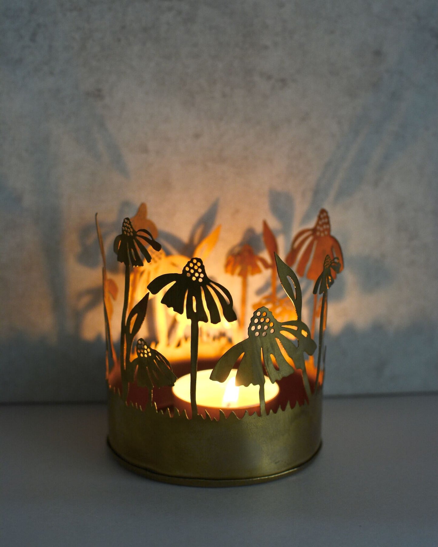 Brass tealight candle holder with floral design, illuminated by candlelight.