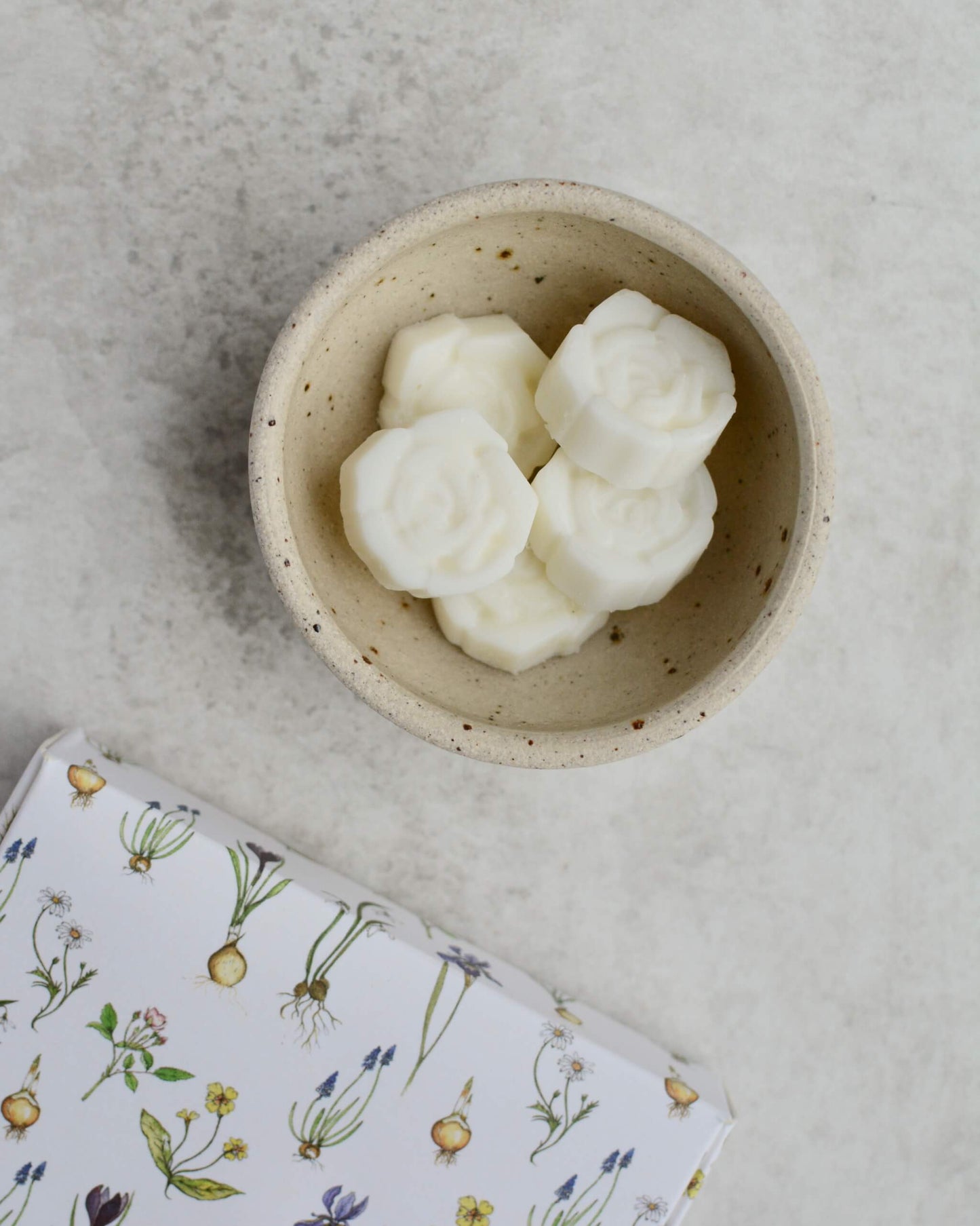 Small bowl with white flower-shaped wax melts, next to an illustrated box.
