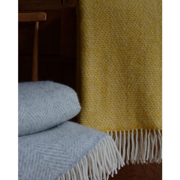 Tweedmill bright yellow beehive wool throw shown next to a folded grey blanket.