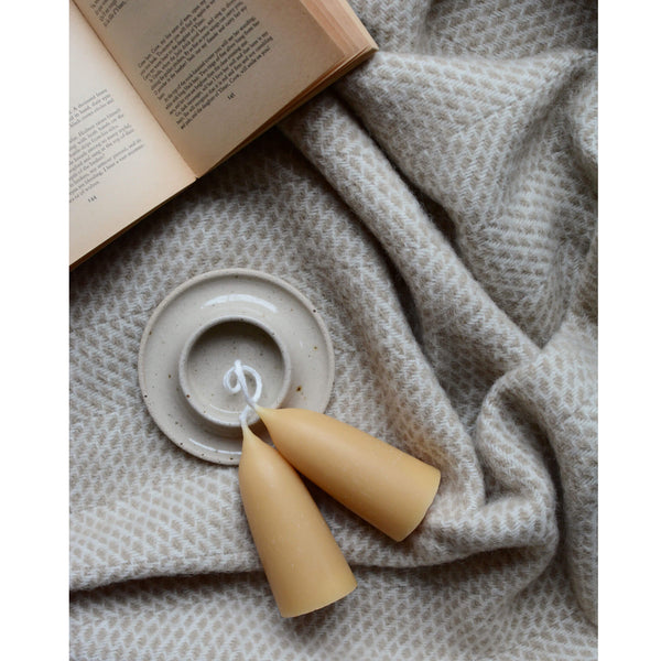 Tweedmill oatmeal beehive wool throw, with a pair of beeswax candles, candle holder and open book.