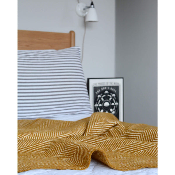 Ochre yellow herringbone wool blanket, shown on a styled bed.
