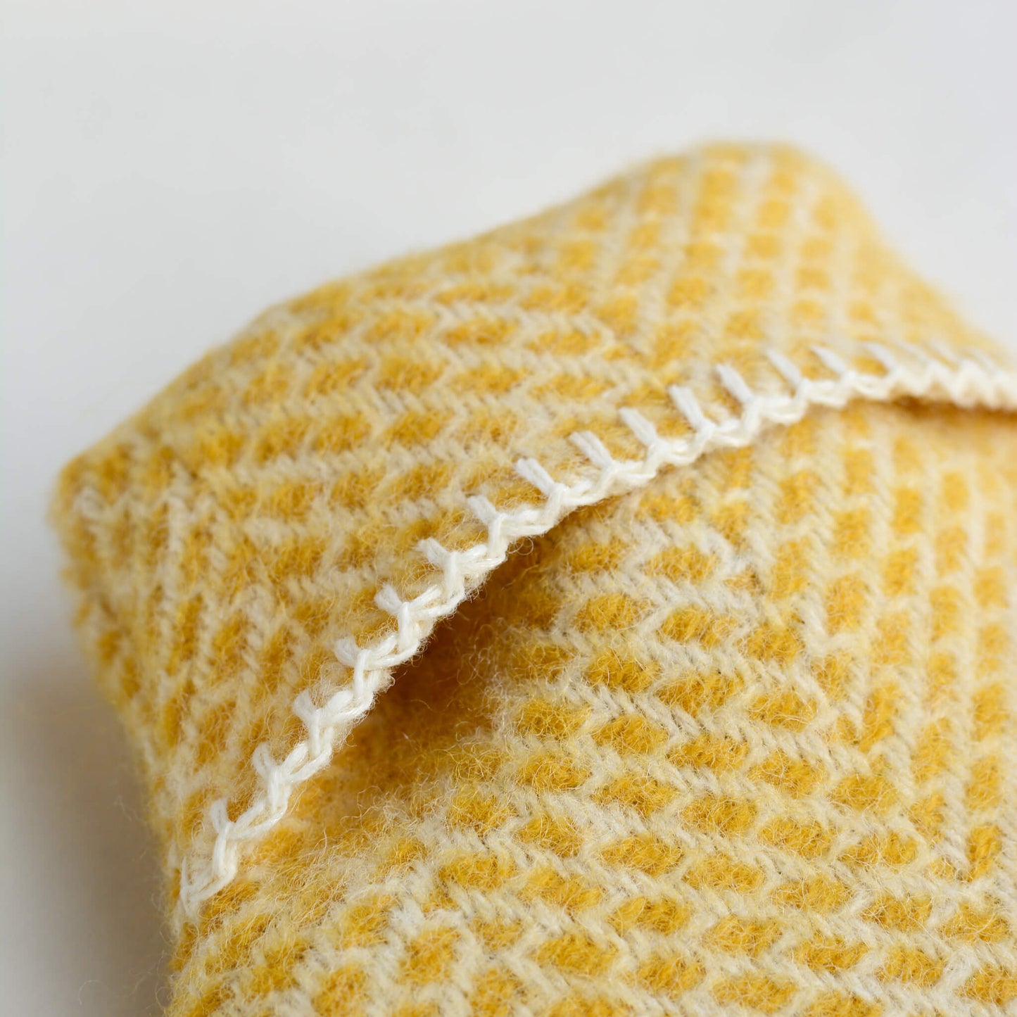 A close up of a bright yellow wool hot water bottle with a beehive pattern, on a white background.