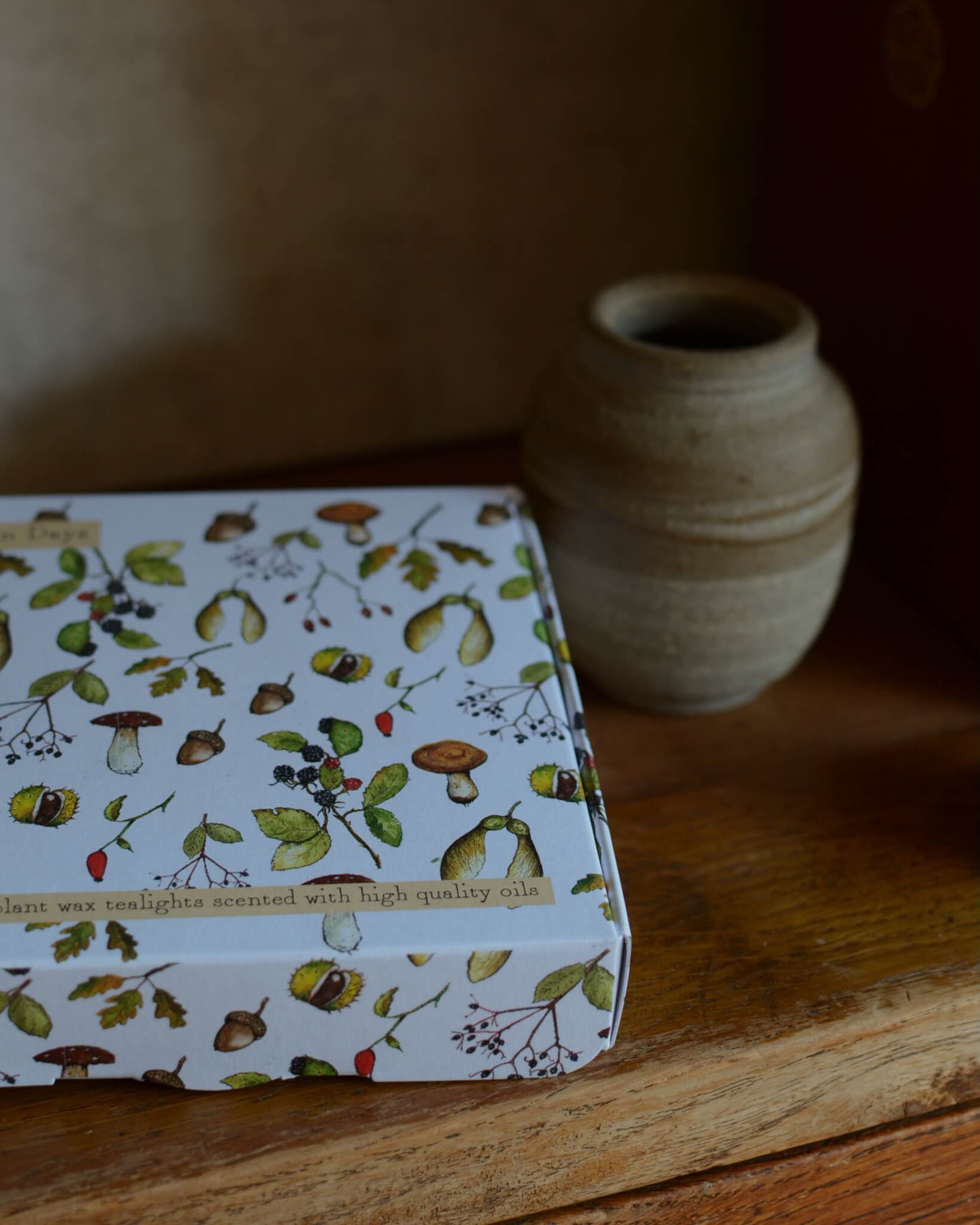 Box of tealights with nature-themed design on a wooden surface with a vase in the background