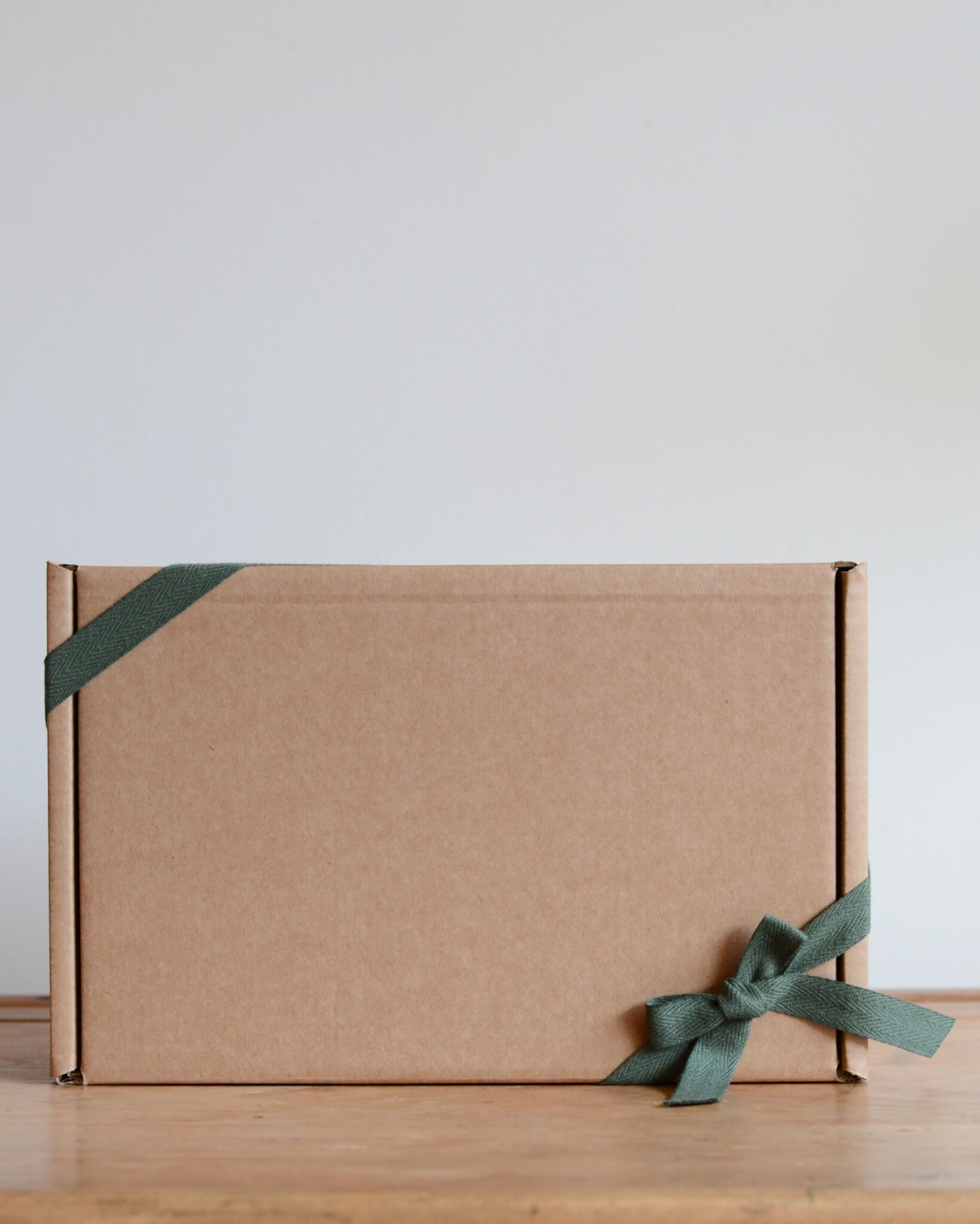 Brown gift box with a green ribbon on a wooden surface.