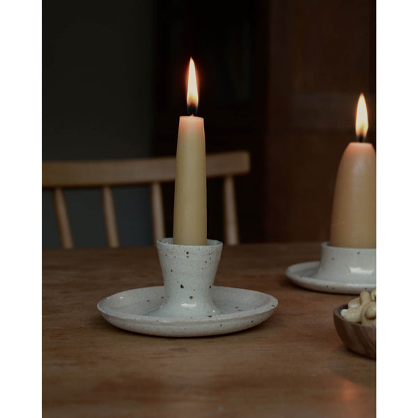 Beeswax taper candles and ceramic candle holder, on a table.