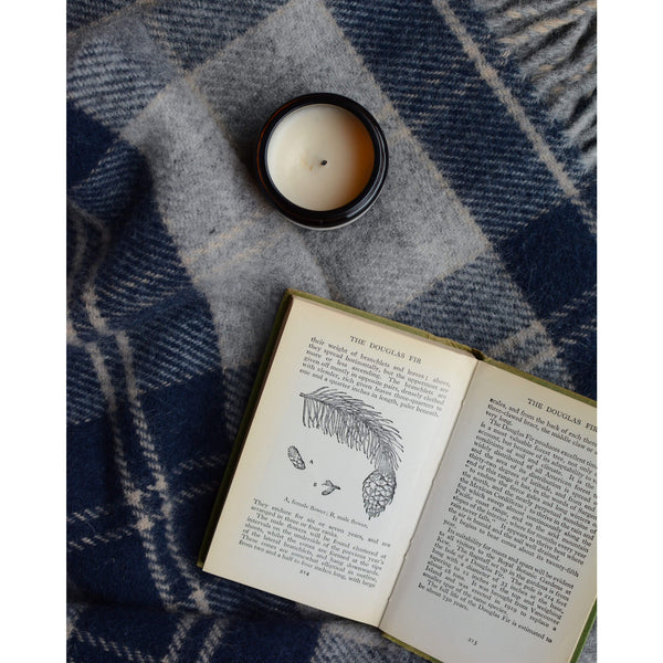 A checked wool blanket in navy and grey with an open book and jar candle.