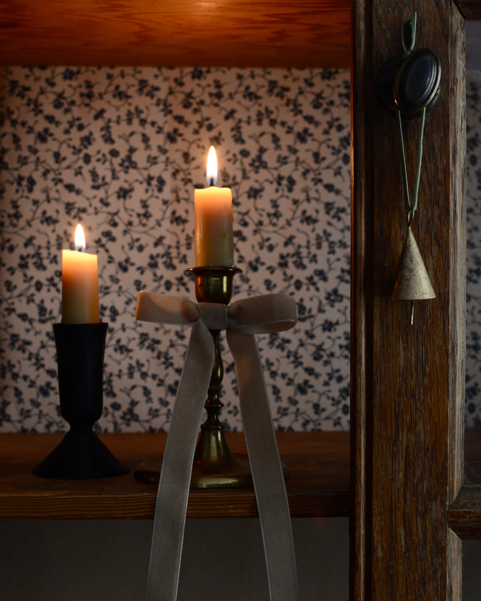 Brass bell Christmas ornament, displayed on a wooden cabinet with lit candles.