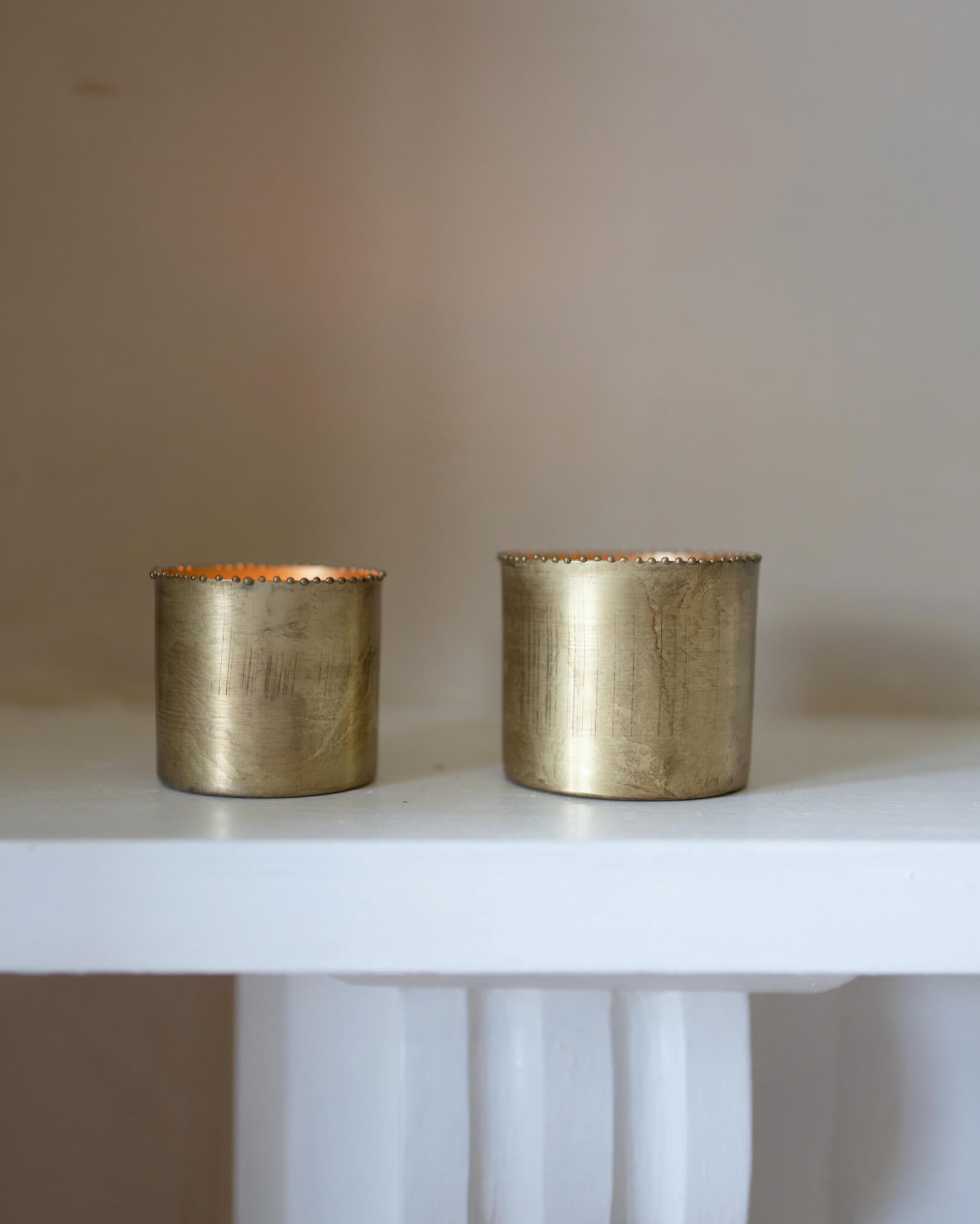 A set of 2 solid brass tea light holders, with beaded detailing around the rim. Shown on a mantlepiece.