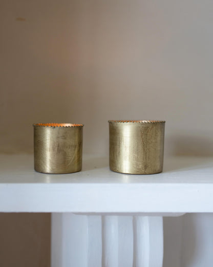A set of 2 solid brass tea light holders, with beaded detailing around the rim. Shown on a mantlepiece.