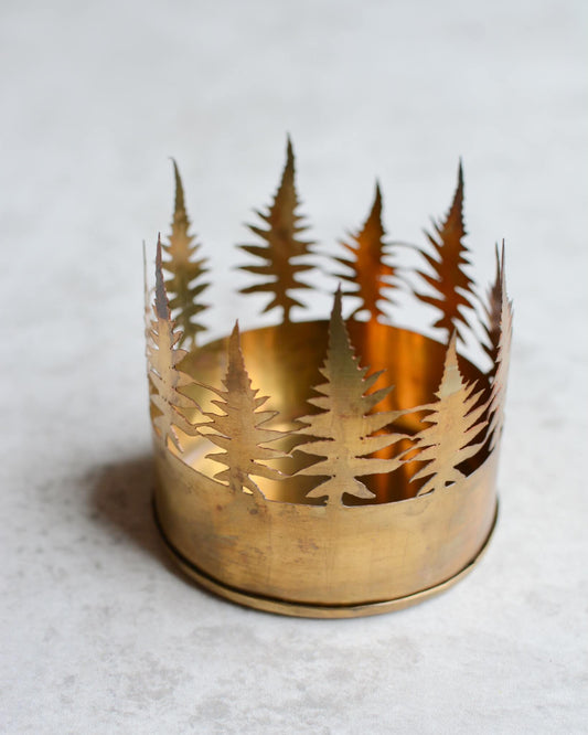 Brass candle holder with cut-out leaf design on a light background.