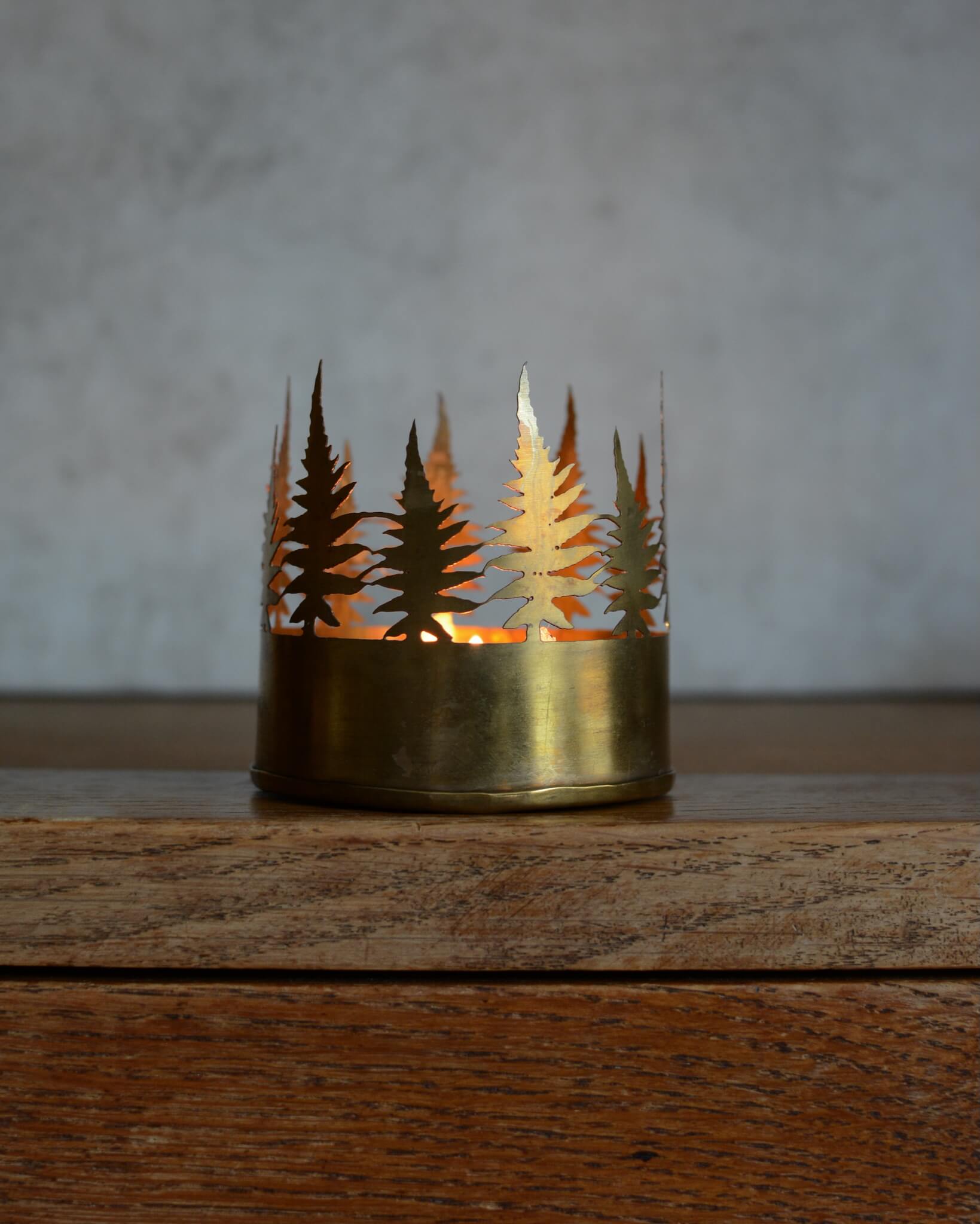 Brass candle holder with cut-out tree design on a wooden surface.
