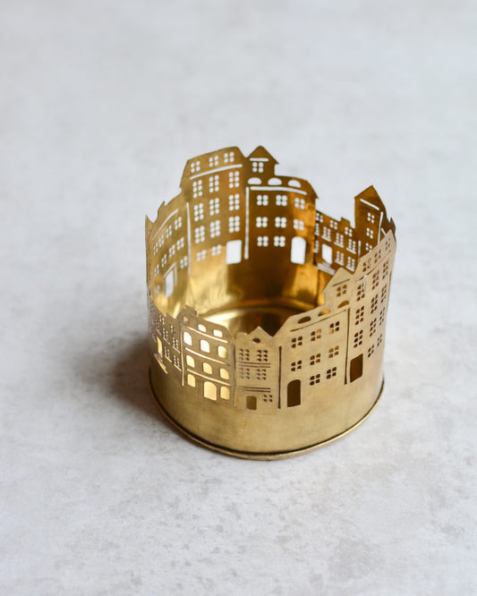 Brass tealight candle holder shaped like a street of townhouses on a white background.