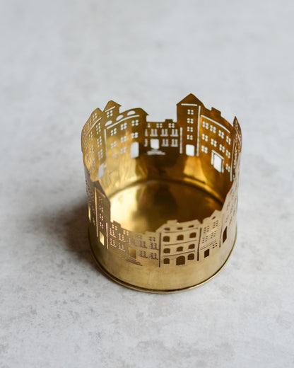 Brass candle holder with cityscape design on a light grey background
