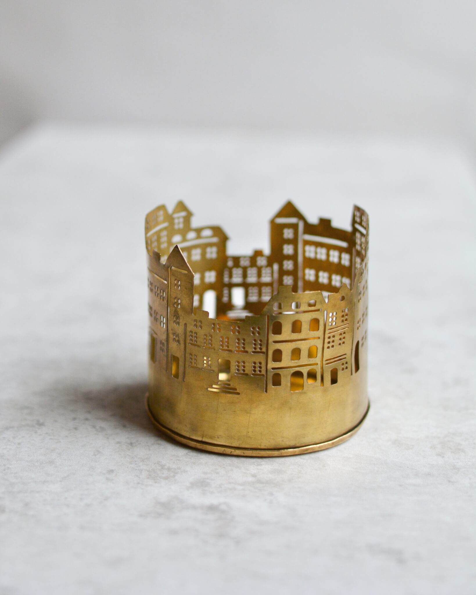 Brass tealight candle holder shaped like a cityscape on a white background.
