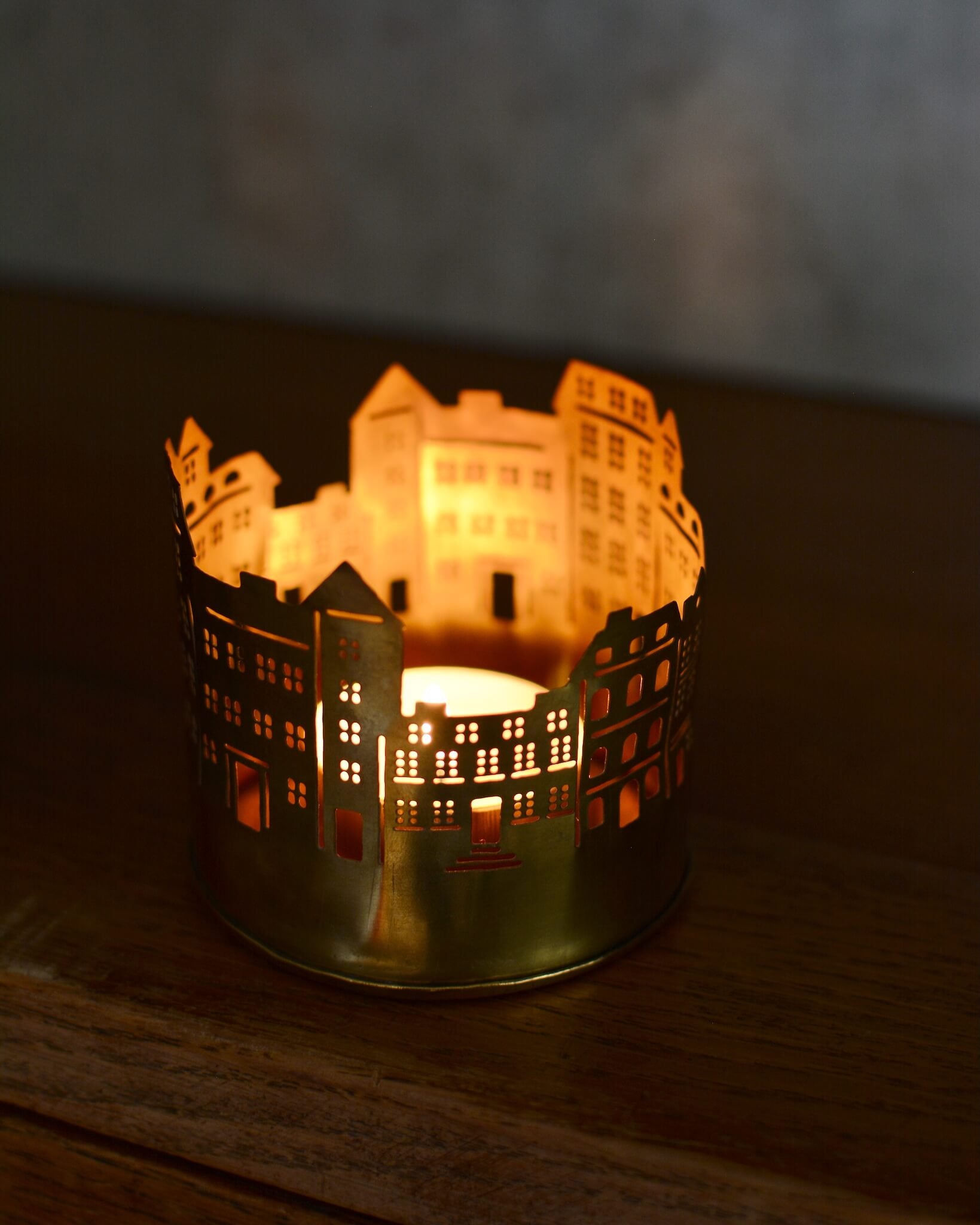 Decorative tealight candle holder with architectural design on a wooden surface.