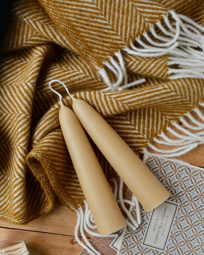 A pair of large stubby beeswax candles on a mustard yellow wool blanket.