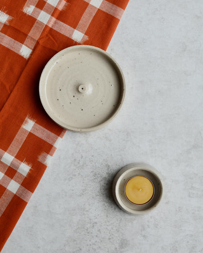 An oatmeal coloured ceramic hand-thrown incense holder, next to a ceramic tealight holder.