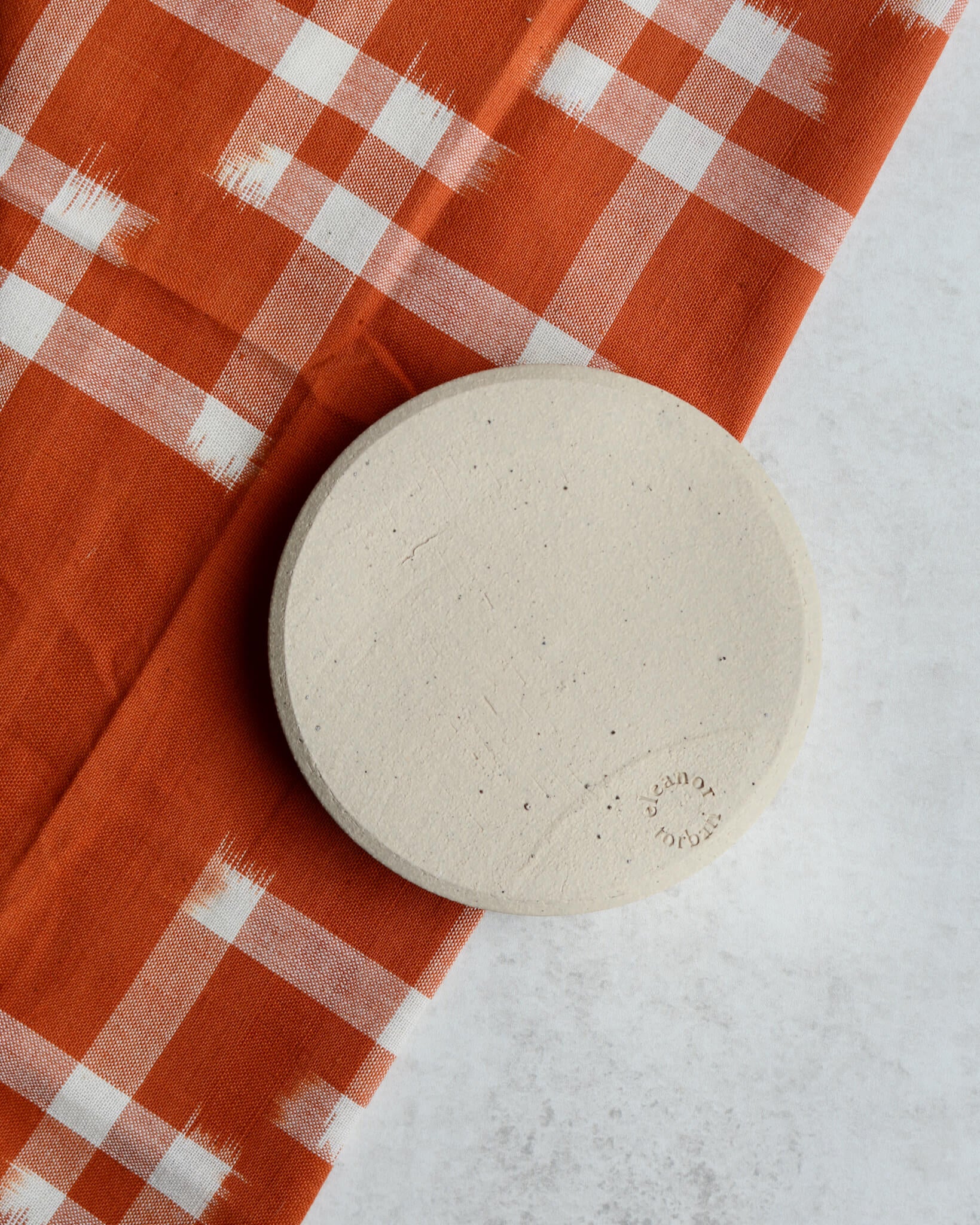 The base of an oatmeal coloured ceramic hand-thrown incense holder, showing the maker's stamp.