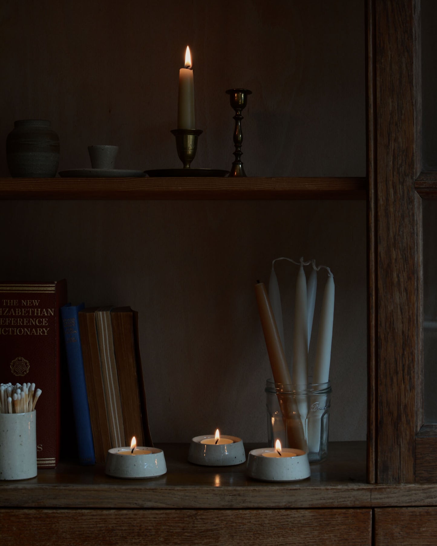 A collection of ceramic tea light holders, shown with lit beeswax tea lights on wooden shelves.