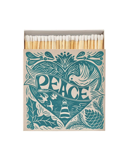 A box of letterpress matches with a Christmas peace theme, featuring a Cornish lighthouse, sea, birds, and festive design on a teal blue background.