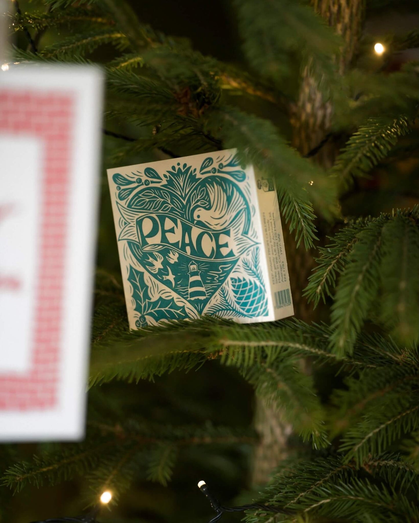 A box of letterpress matches with a Christmas peace theme, shown nestled in a Christmas fir tree.