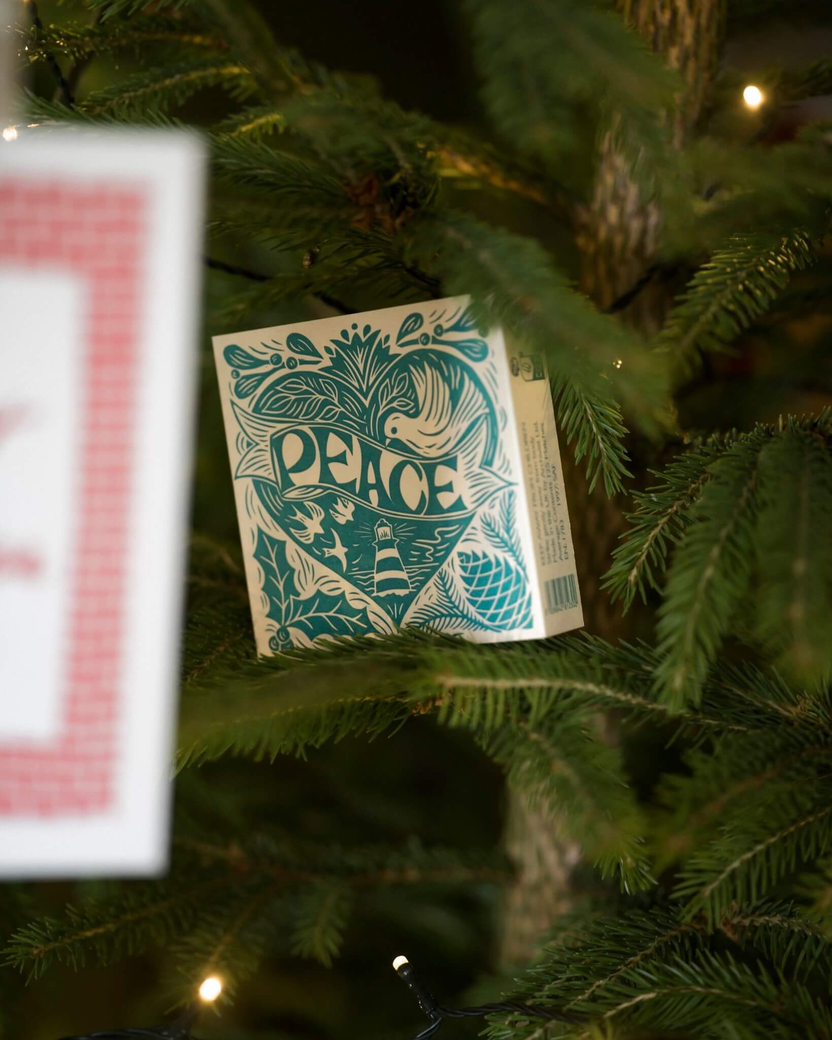 A box of letterpress matches with a Christmas peace theme, shown nestled in a Christmas fir tree.
