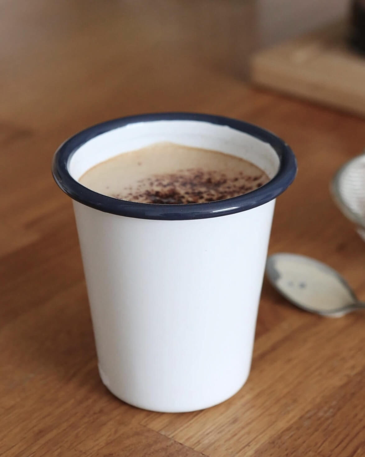 A classic white enamel tumbler with navy rim, with hot chocolate inside.