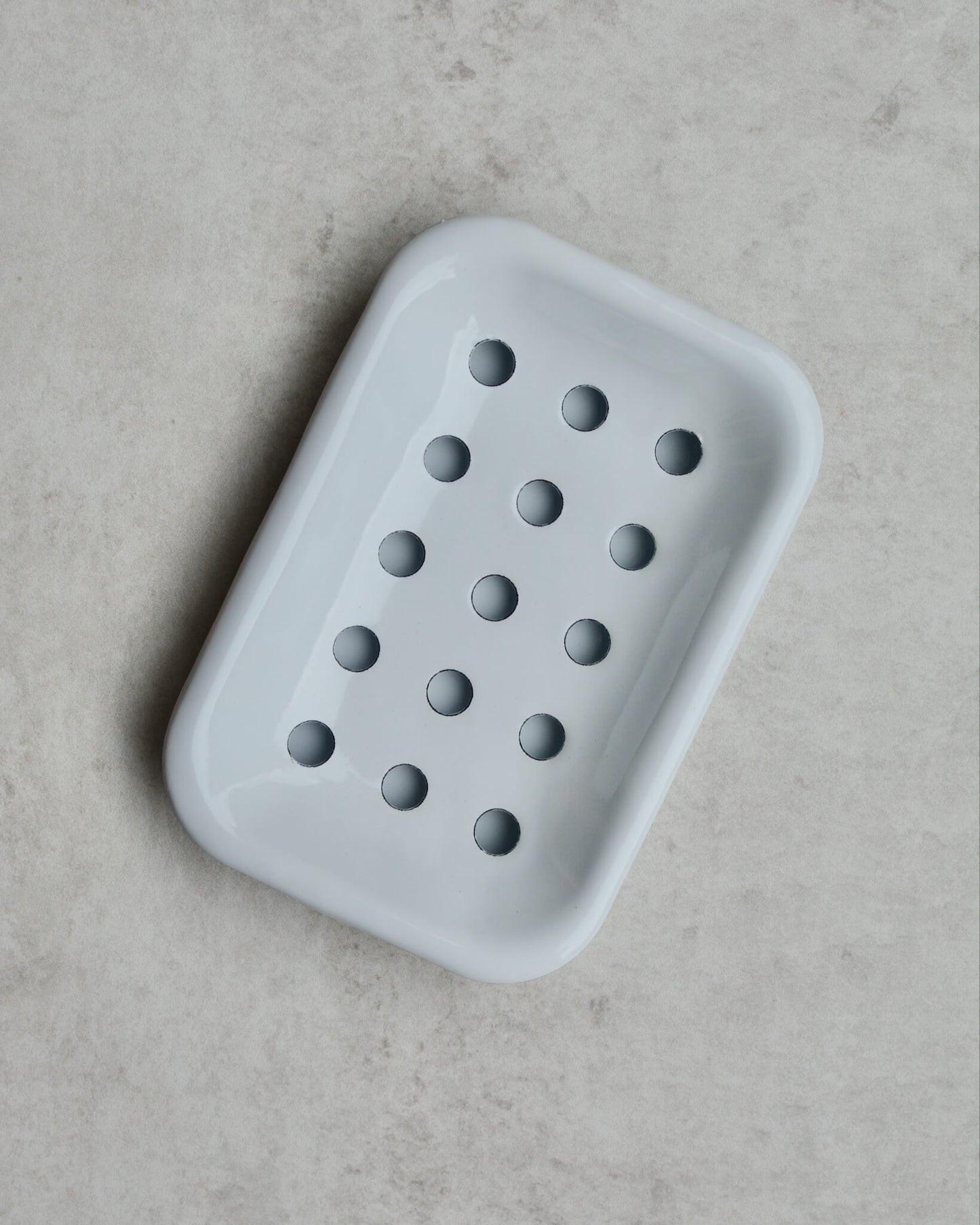 White enamel soap dish with drip tray on a grey background.
