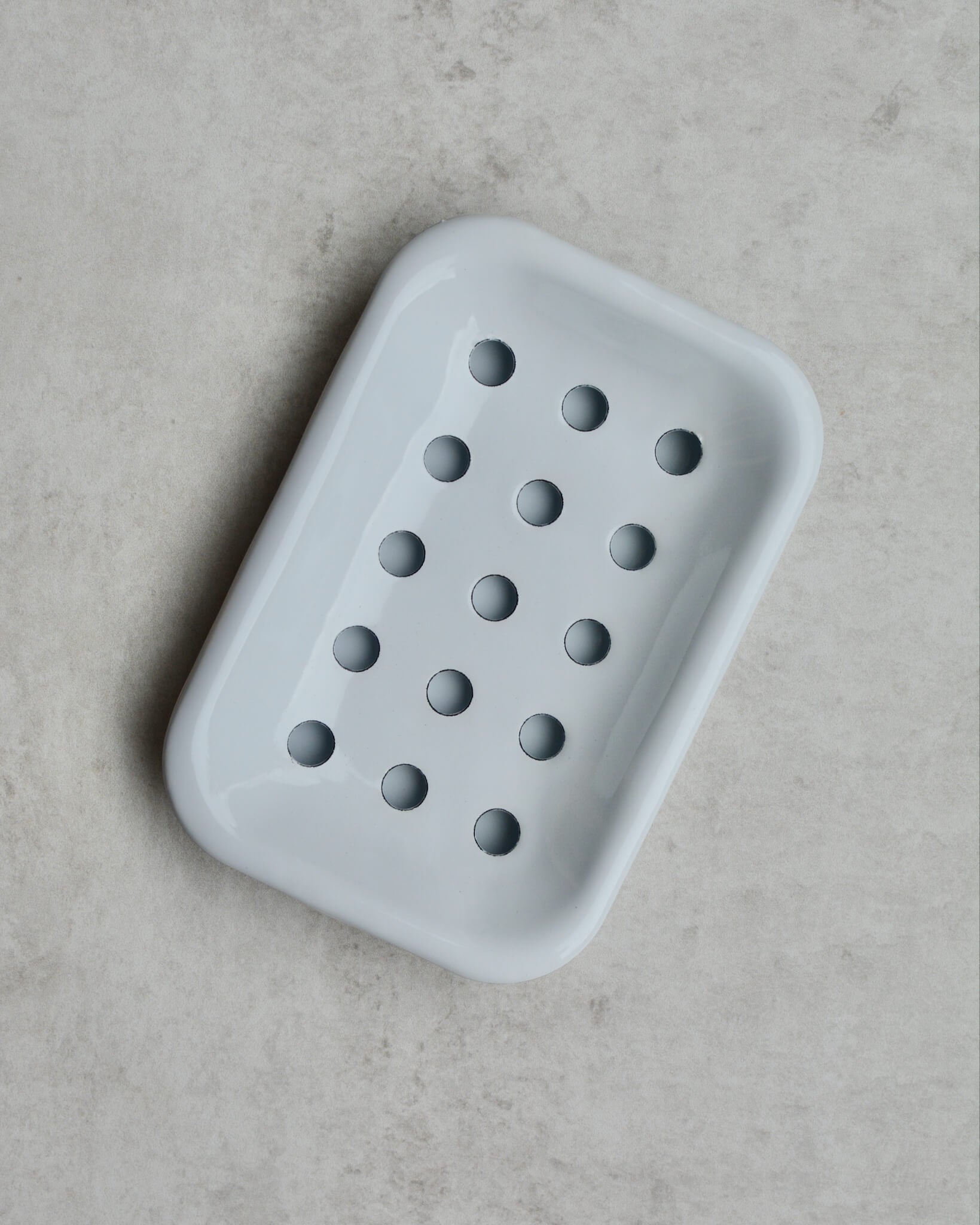 White enamel soap dish with drip tray on a grey background.