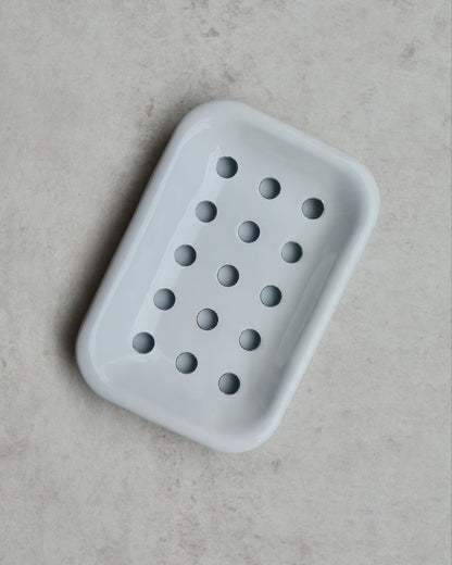 White enamel soap dish with drip tray on a grey background.