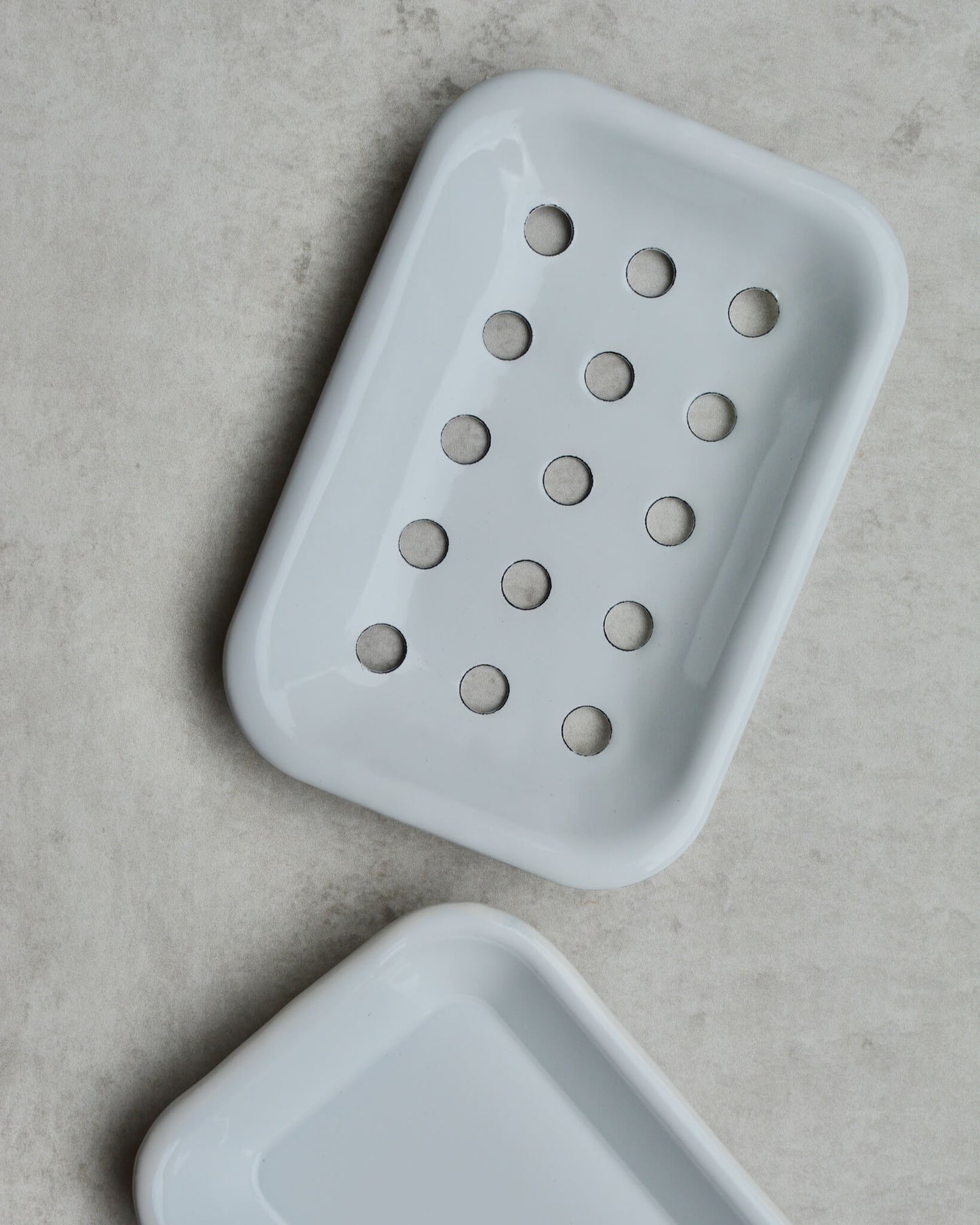 White enamel soap dish with drip tray on a grey background.