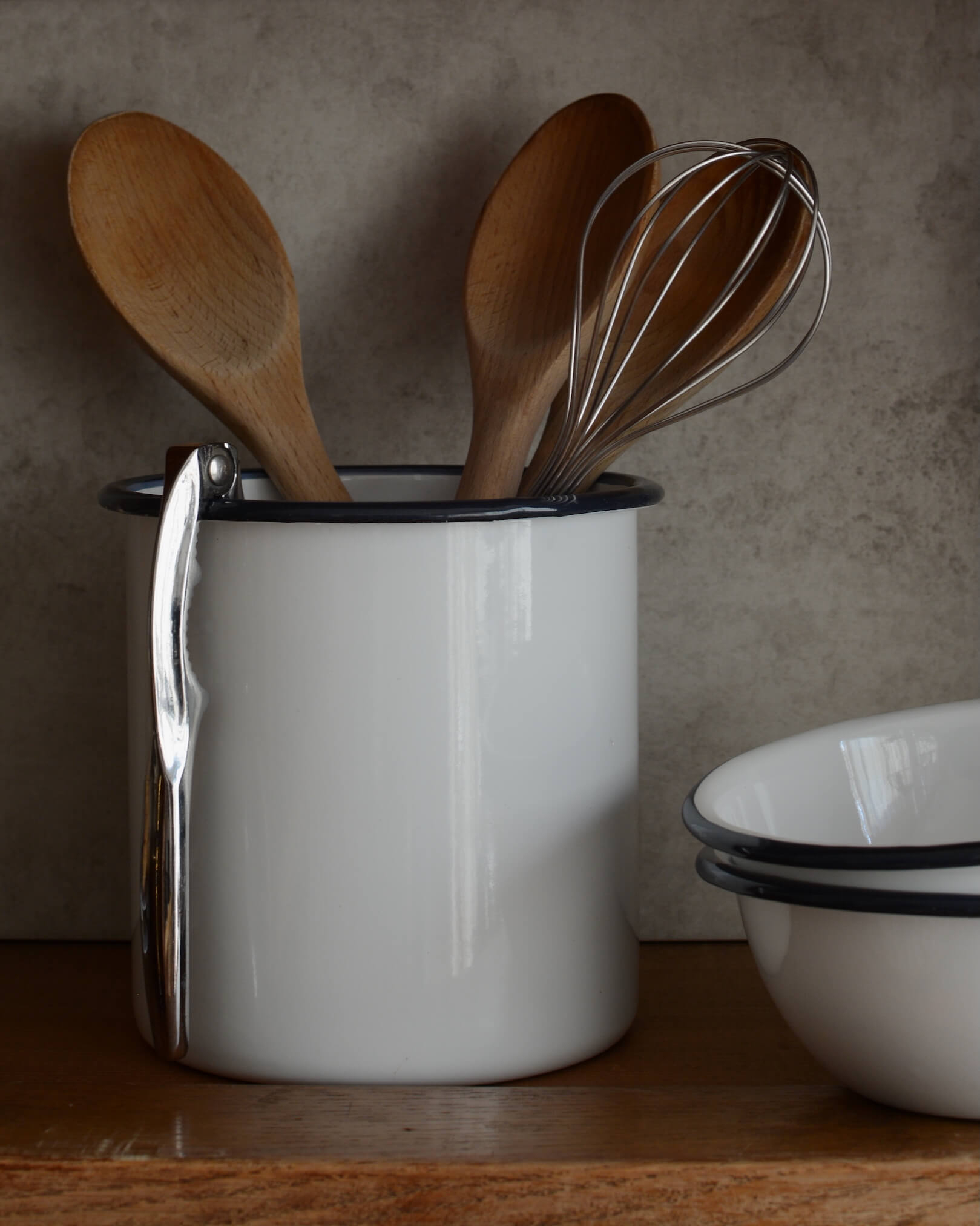A white enamel utensil holder, filled with wooden spoons and other kitchen utensils.