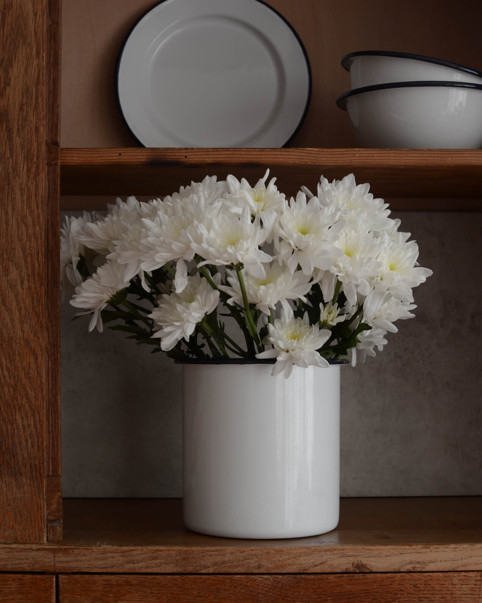 A white enamel utensil holder, used as a cut flower vase, with white flowers.