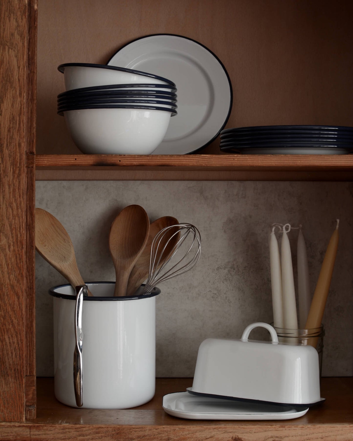 A collection of white and navy enamelware, with bowls, plates utensil holder and butter dish.
