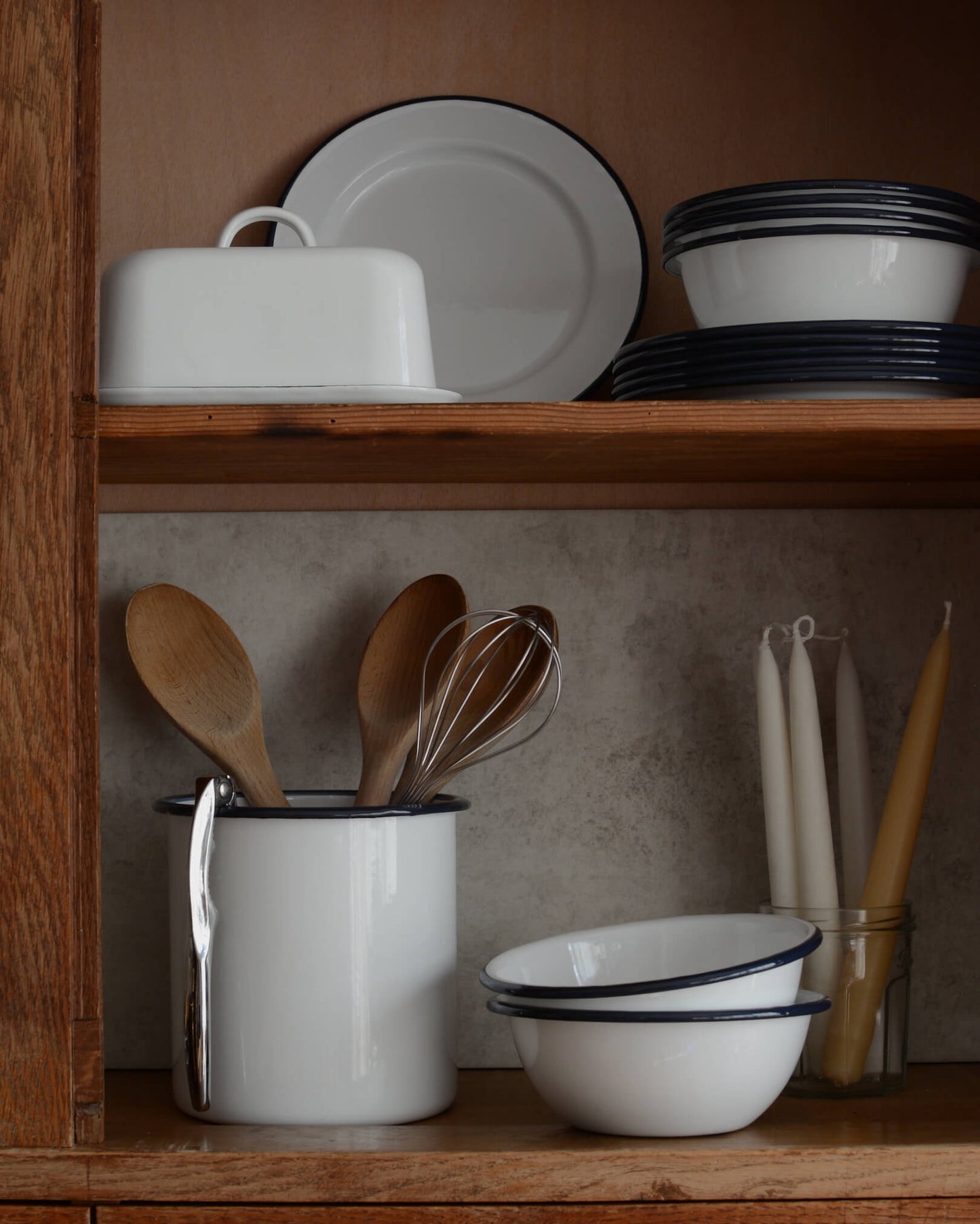A collection of white and navy enamelware, with bowls, plates utensil holder and butter dish.
