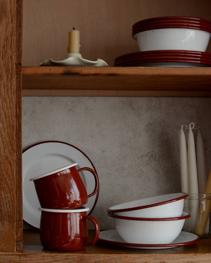 A collection of white and burgundy red enamel bowls, plates and cups.