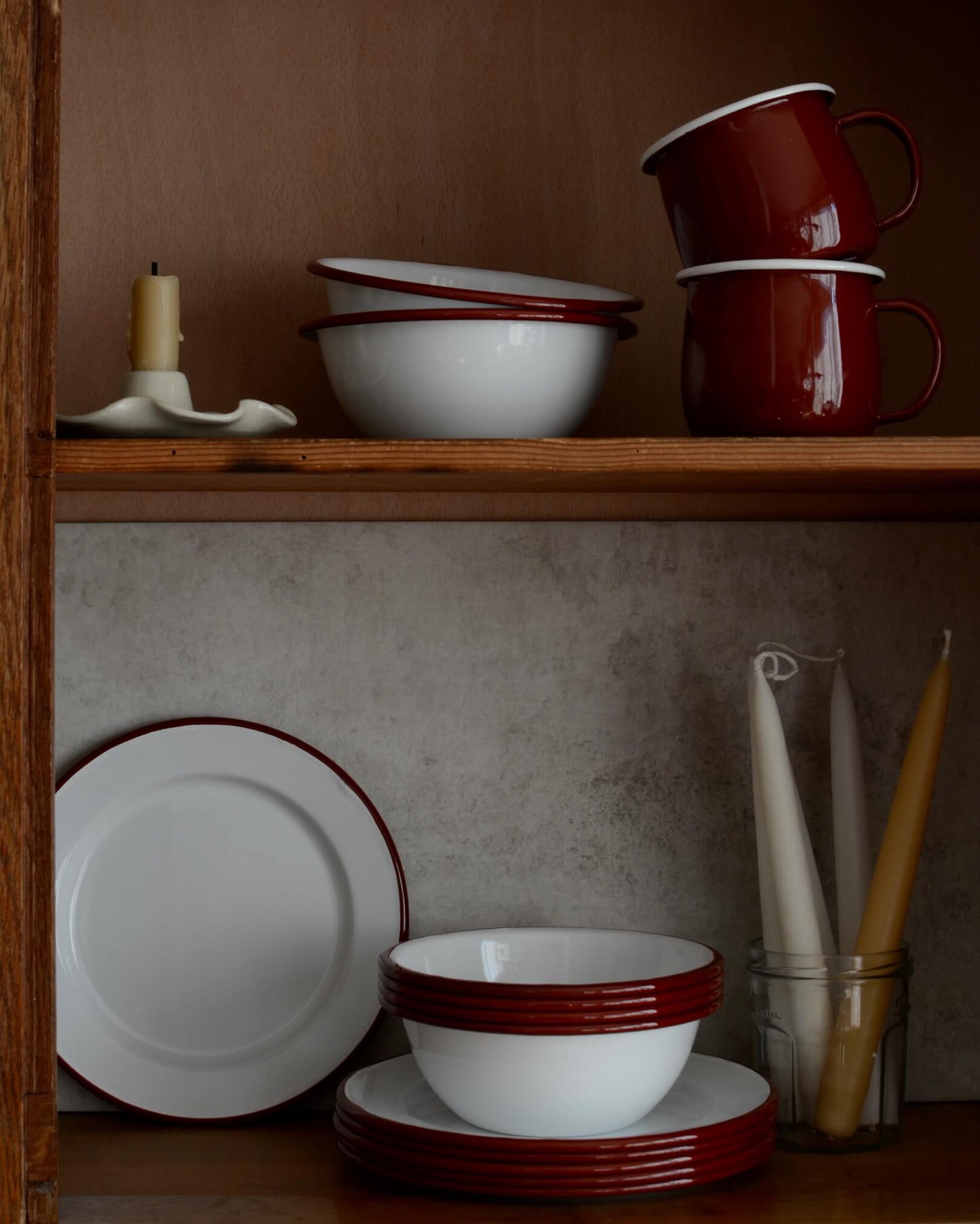 A collection of white and burgundy red enamel bowls, plates and cups.