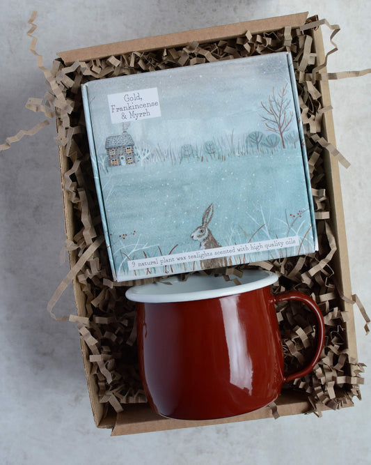 Red mug and illustrated box of tealight candles in a gift box with crinkled paper.