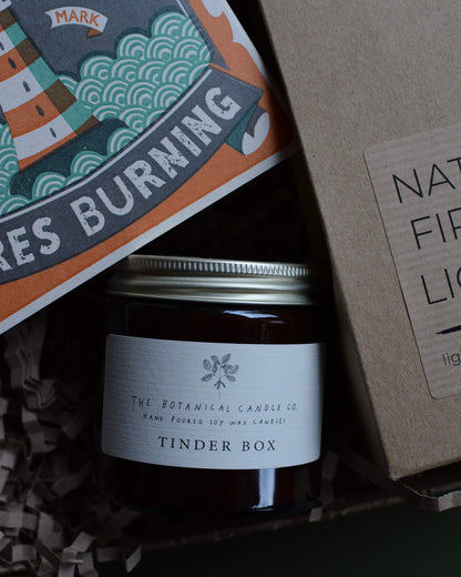 Gift box, containing an amber jar candle, box of matches with a lighthouse design and a pack of natural firelighters.