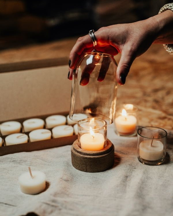 Hand placing a glass over a lit candle with more candles and a box in the background