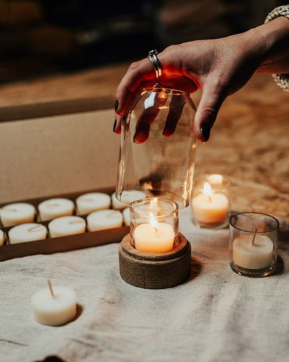 Hand placing a glass over a lit candle with more candles and a box in the background