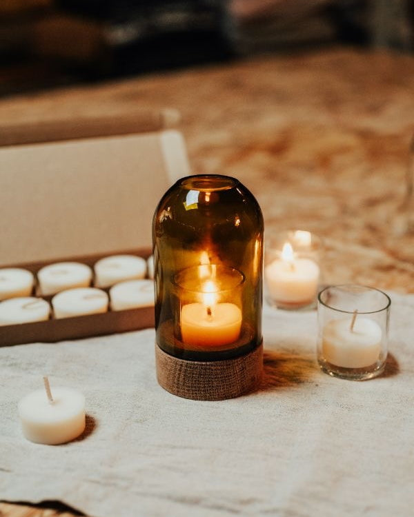 Candle in an olive green glass holder on a textured surface with other candles.