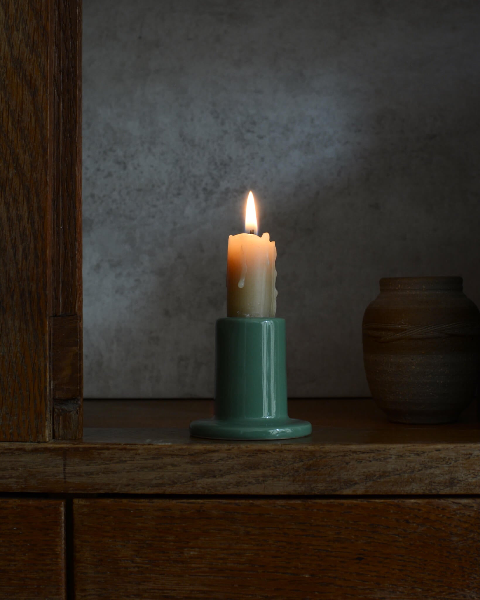 A beeswax candle in a green ceramic holder, on a wooden surface with a dark background
